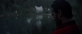 Movie still from “The Sisters Brothers” (2018), directed by Jacques Audiard – A man standing in front of a body of water at night; Close Up shot, Over the shoulder angle