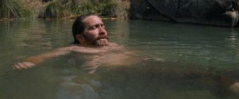 Movie still from “The Sisters Brothers” (2018), directed by Jacques Audiard – A man with long hair and a beard swimming in a body of water; Medium shot, High angle
