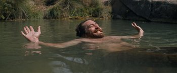 Movie still from “The Sisters Brothers” (2018), directed by Jacques Audiard – A man with a beard is swimming in a body of water; Medium shot, High angle