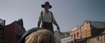 Movie still from “The Sisters Brothers” (2018), directed by Jacques Audiard – An old man in a hat and a brown hat is holding a gun; Medium shot, Over the shoulder angle