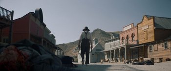 Movie still from “The Sisters Brothers” (2018), directed by Jacques Audiard – A man walking down a street with a hat on; Wide shot, Low angle
