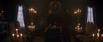 Movie still from “The Sisters Brothers” (2018), directed by Jacques Audiard – Two men standing next to a table in a dark room; Wide shot, Over the shoulder angle