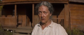 Movie still from “The Sisters Brothers” (2018), directed by Jacques Audiard – An older woman with a white shirt and grey hair looking at the camera; Close Up shot, Low angle