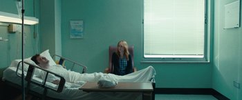 Movie still from “The Skeleton Twins” (2014), directed by Craig Johnson – A woman sitting in a chair next to a bed in a hospital room; Wide shot, Over the shoulder angle