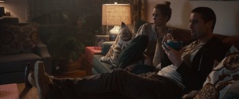 Movie still from “The Skeleton Twins” (2014), directed by Craig Johnson – A woman sitting on top of a couch next to a cat pillow; Medium shot, Over the shoulder angle
