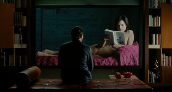 Movie still from “The Skin I Live In” (2011), directed by Pedro Almodóvar – A man sitting in front of a woman reading a book; Medium shot, Over the shoulder angle