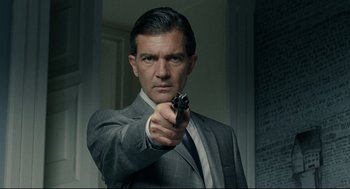 Movie still from “The Skin I Live In” (2011), directed by Pedro Almodóvar – A man in a suit and tie holding a gun; Close Up shot, Over the shoulder angle
