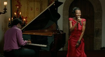 Movie still from “The Skin I Live In” (2011), directed by Pedro Almodóvar – A woman in a red dress is singing next to a grand piano; Medium shot, Low angle