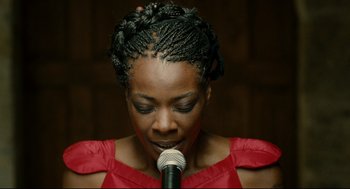 Movie still from “The Skin I Live In” (2011), directed by Pedro Almodóvar – A woman in a red dress is holding a microphone; Close Up shot, Overhead angle