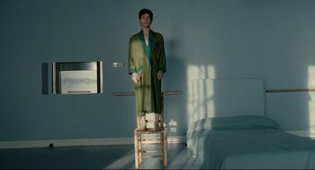 Movie still from “The Skin I Live In” (2011), directed by Pedro Almodóvar – A man standing on top of a chair in a room; Wide shot, Low angle
