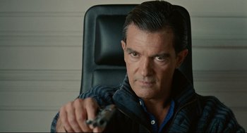 Movie still from “The Skin I Live In” (2011), directed by Pedro Almodóvar – A person sitting in a chair holding a gun; Close Up shot, Over the shoulder angle