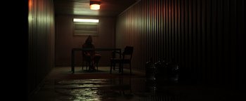 Movie still from “Sicario: Day of the Soldado” (2018), directed by Stefano Sollima – A person sitting at a table in a dark room; Wide shot, Low angle
