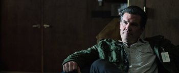 Movie still from “Sicario: Day of the Soldado” (2018), directed by Stefano Sollima – A man sitting on a couch wearing a green jacket; Close Up shot, Over the shoulder angle