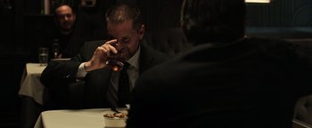 Movie still from “Sicario: Day of the Soldado” (2018), directed by Stefano Sollima – A man in a suit and tie drinking from a glass; Medium shot, Over the shoulder angle