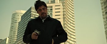 Movie still from “Sicario: Day of the Soldado” (2018), directed by Stefano Sollima – A man holding a camera while standing in front of a tall building; Medium shot, Low angle