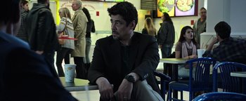 Movie still from “Sicario: Day of the Soldado” (2018), directed by Stefano Sollima – A man in a suit sitting at a table with other people; Medium shot, Over the shoulder angle