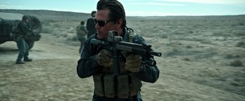Movie still from “Sicario: Day of the Soldado” (2018), directed by Stefano Sollima – A man holding a gun while standing in the desert; Medium shot, Over the shoulder angle