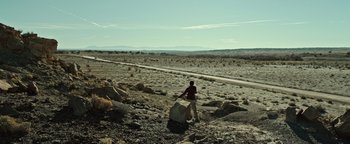 Movie still from “Sicario: Day of the Soldado” (2018), directed by Stefano Sollima – A man is walking through the desert with a large piece of rock; Extreme Wide shot, Low angle