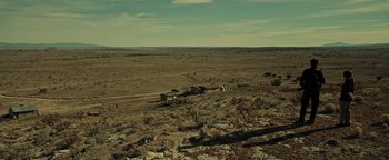 Movie still from “Sicario: Day of the Soldado” (2018), directed by Stefano Sollima – An empty field with a few buildings in the distance; Extreme Wide shot, High angle