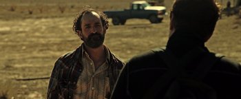 Movie still from “Sicario: Day of the Soldado” (2018), directed by Stefano Sollima – A man with a beard is standing in a field; Close Up shot, Over the shoulder angle