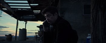 Movie still from “Sicario: Day of the Soldado” (2018), directed by Stefano Sollima – A man talking on a cell phone while sitting down; Medium shot, Low angle