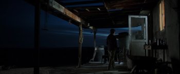 Movie still from “Sicario: Day of the Soldado” (2018), directed by Stefano Sollima – A man standing under a wooden structure at night; Wide shot, Low angle