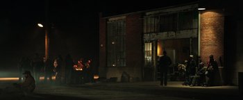 Movie still from “Sicario: Day of the Soldado” (2018), directed by Stefano Sollima – A group of people standing in front of a brick building at night; Extreme Wide shot, Over the shoulder angle