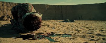 Movie still from “Sicario: Day of the Soldado” (2018), directed by Stefano Sollima – A person is walking in the sand with a bag of trash; Medium shot, High angle