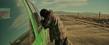 Movie still from “Sicario: Day of the Soldado” (2018), directed by Stefano Sollima – A man leaning on the side of a green car on the side of the road; Medium shot, Over the shoulder angle