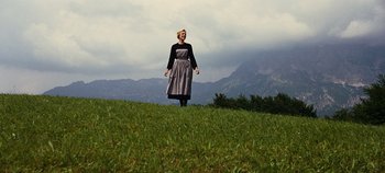 Movie still from “The Sound of Music” (1965), directed by Robert Wise – A woman standing on top of a grass covered hill; Wide shot, Low angle