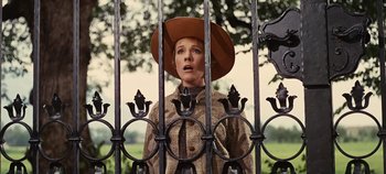 Movie still from “The Sound of Music” (1965), directed by Robert Wise – A woman with a hat standing in front of an iron gate; Medium shot, Low angle