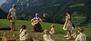 Movie still from “The Sound of Music” (1965), directed by Robert Wise – A group of people sitting in a field with mountains in the background; Wide shot, High angle