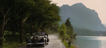 Movie still from “The Sound of Music” (1965), directed by Robert Wise – A couple of cars driving down a road next to a body of water; Extreme Wide shot, High angle