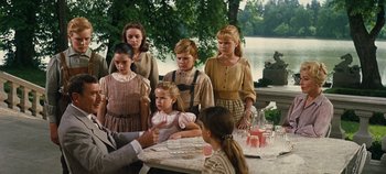Movie still from “The Sound of Music” (1965), directed by Robert Wise – A group of people standing around a table; Medium shot, Over the shoulder angle