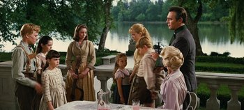 Movie still from “The Sound of Music” (1965), directed by Robert Wise – A group of people standing around a table with a lake in the background; Medium shot, Over the shoulder angle