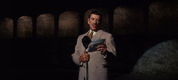 Movie still from “The Sound of Music” (1965), directed by Robert Wise – A man in a suit and tie holding a microphone; Medium shot, High angle