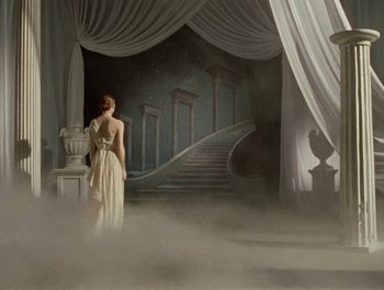 A woman in a white dress standing in front of a staircase