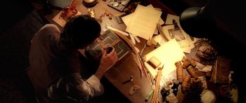 Movie still from “The Spiderwick Chronicles” (2008), directed by Mark Waters – A man working at a table with papers and a lamp; Medium shot, Overhead angle