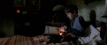 Movie still from “The Spiderwick Chronicles” (2008), directed by Mark Waters – A young boy sitting on a bed looking at an open book; Medium shot, High angle