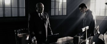 Movie still from “The Spirit” (2008), directed by Frank Miller – A man standing in front of a laptop computer; Medium shot, Low angle