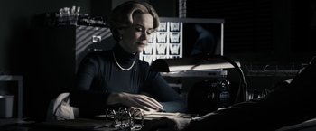 Movie still from “The Spirit” (2008), directed by Frank Miller – A woman sitting at a table with a lamp; Medium shot, Over the shoulder angle