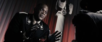 Movie still from “The Spirit” (2008), directed by Frank Miller – A man in a military uniform is standing in front of a statue of an eagle; Close Up shot, High angle