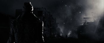 Movie still from “The Spirit” (2008), directed by Frank Miller – A man standing on a street at night with smoke billowing out of the sky; Wide shot, Low angle
