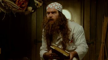 Movie still from “The SpongeBob Movie: Sponge Out of Water” (2015), directed by Mike Mitchell – A man with long hair and a beard holding an old book; Medium shot, Low angle