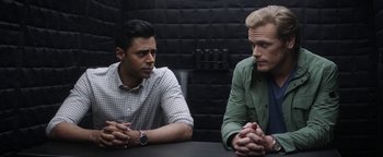 Movie still from “The Spy Who Dumped Me” (2018), directed by Susanna Fogel – Two men sitting at a table with their hands crossed; Medium shot, Over the shoulder angle