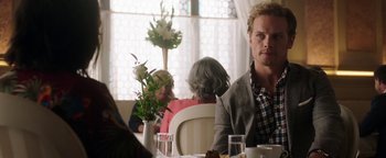 Movie still from “The Spy Who Dumped Me” (2018), directed by Susanna Fogel – A man sitting at a table with a bunch of flowers in front of him; Medium shot, Over the shoulder angle