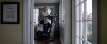 Movie still from “The Spy Who Dumped Me” (2018), directed by Susanna Fogel – An older man riding an exercise bike in a room; Wide shot, Low angle
