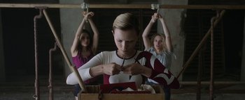 Movie still from “The Spy Who Dumped Me” (2018), directed by Susanna Fogel – A woman is cutting a piece of paper while two other women watch; Medium shot, Low angle
