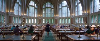 Movie still from “The Spy Who Dumped Me” (2018), directed by Susanna Fogel – A woman walking through a library filled with tables and chairs; Wide shot, Low angle