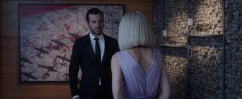 Movie still from “The Spy Who Dumped Me” (2018), directed by Susanna Fogel – A man in a suit and tie standing next to a woman in a purple dress; Medium shot, Over the shoulder angle